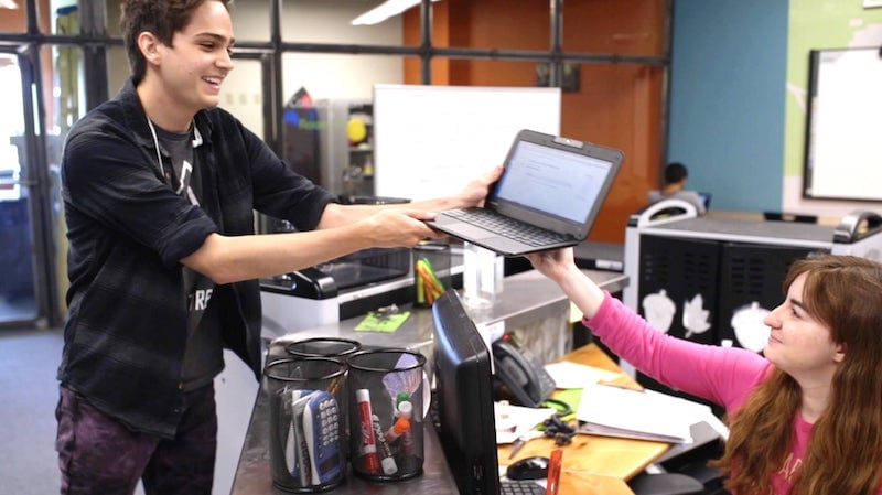 high school student receiving personal computer from teacher